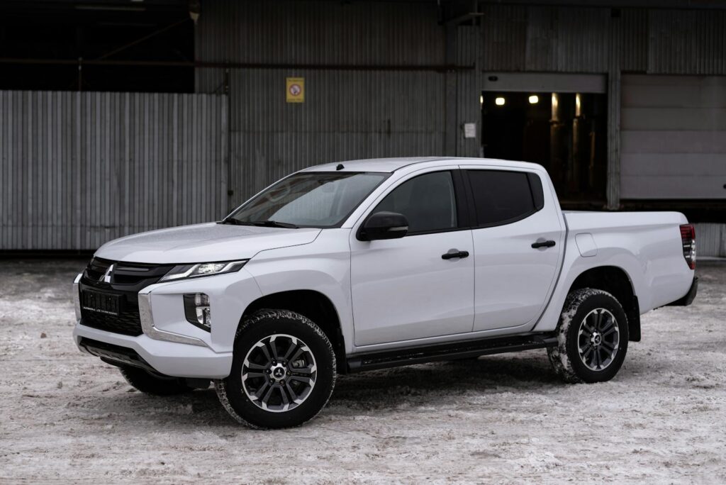 Modern white Mitsubishi pickup truck parked on snow, showcasing sleek design and winter-ready capabilities.