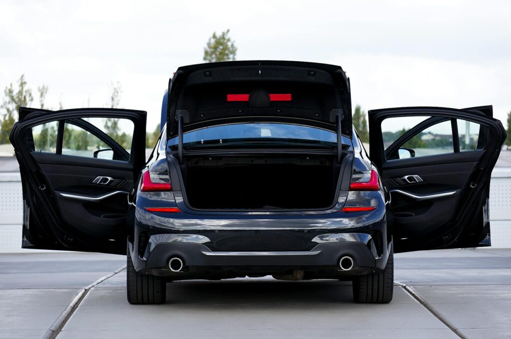 Rear view of a modern black car with open doors and trunk, showcasing its stylish design.