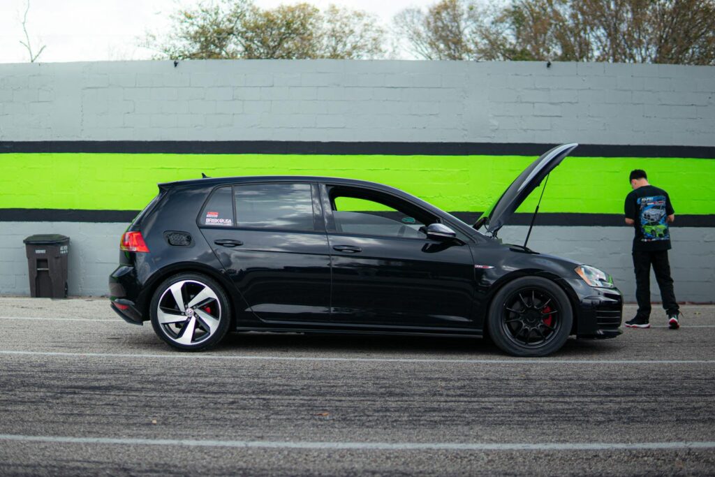 Side view of a black Volkswagen Golf GTI with hood open, parked on roadside.