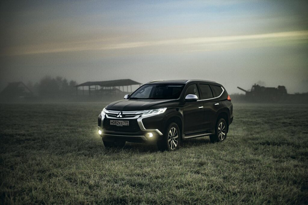 A black Mitsubishi SUV stationed in a misty field during twilight, headlights on.
