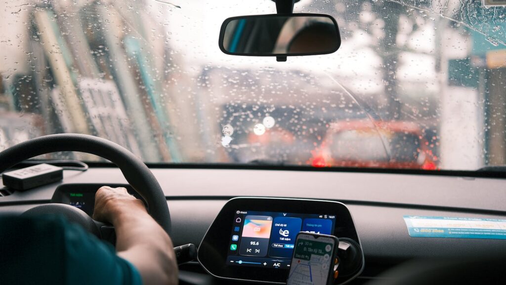 Interior view of a car during a rainy drive in city traffic, focus on dashboard and windshield.