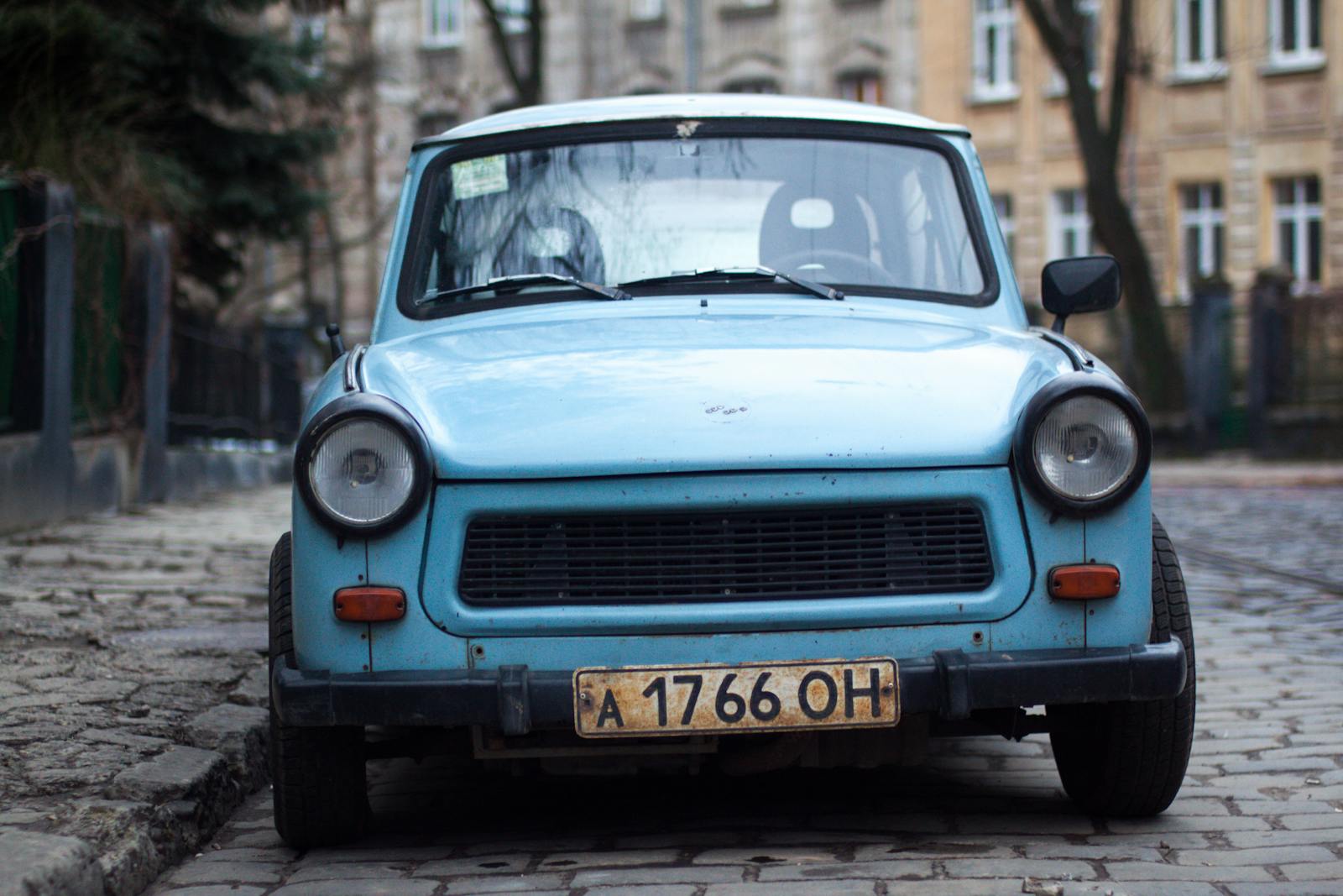 Front view of a classic vintage blue car parked on a cobblestone street in an urban setting.