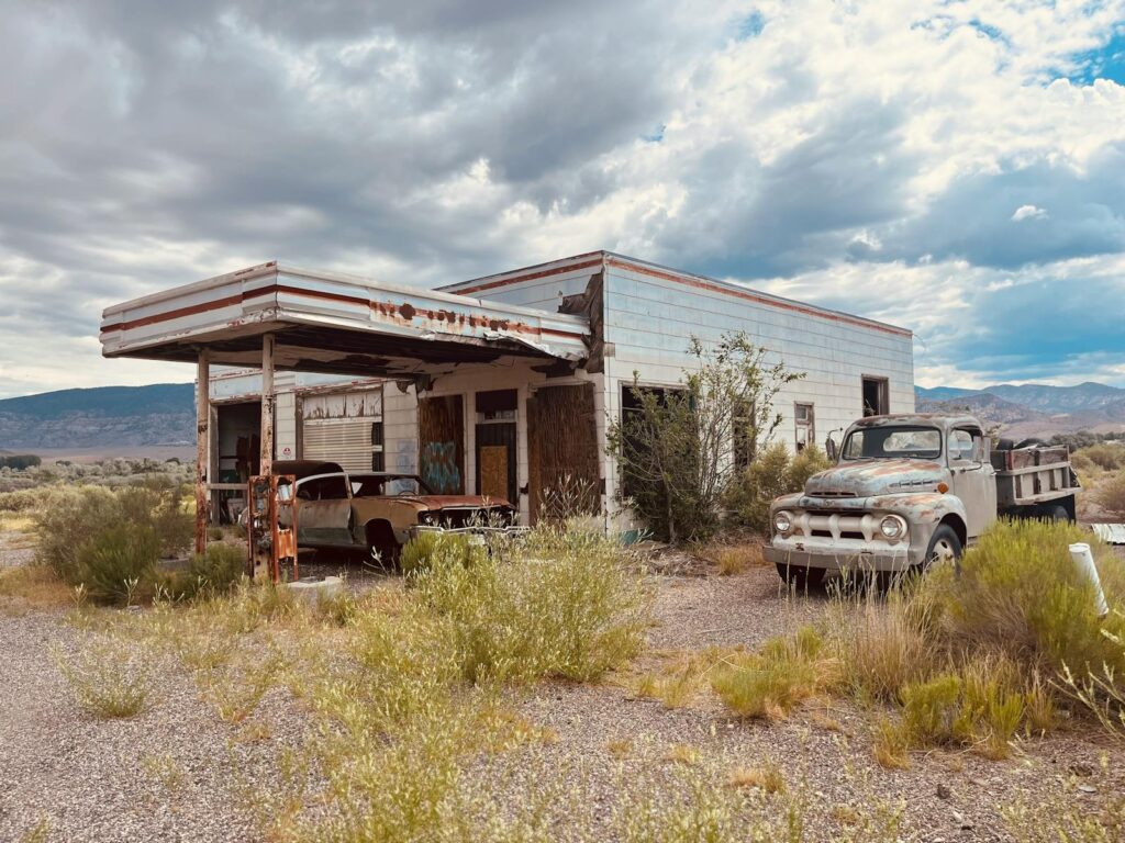 Rustic abandoned gas station with vintage cars in a desert landscape.