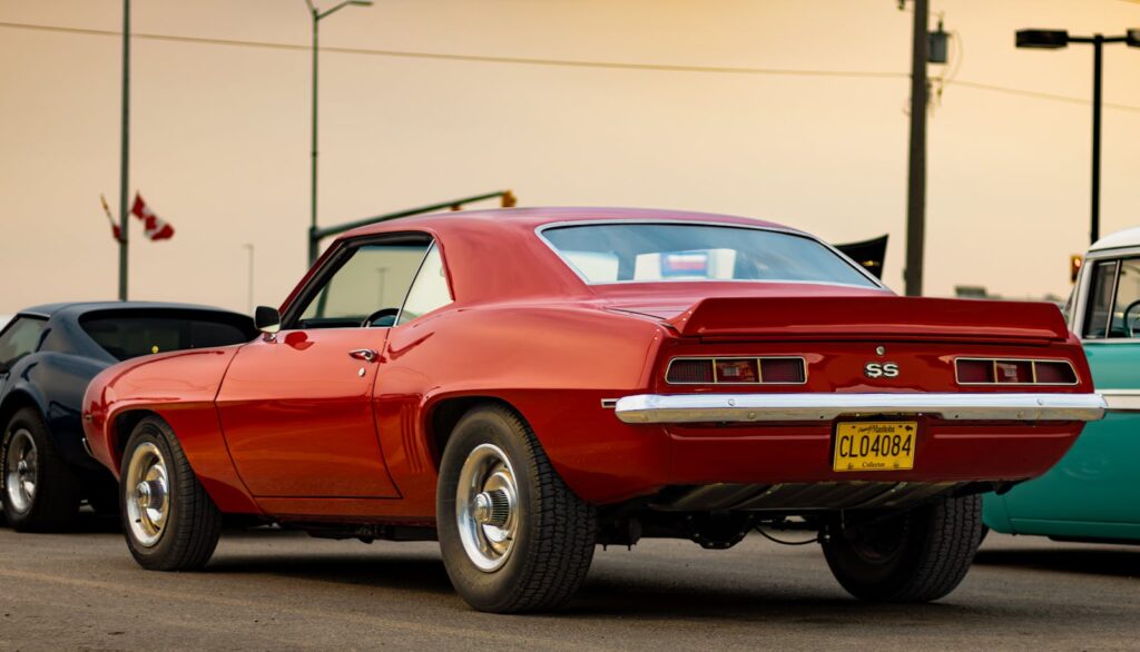 A red Chevrolet Camaro SS parked alongside other vintage cars at a car show event.