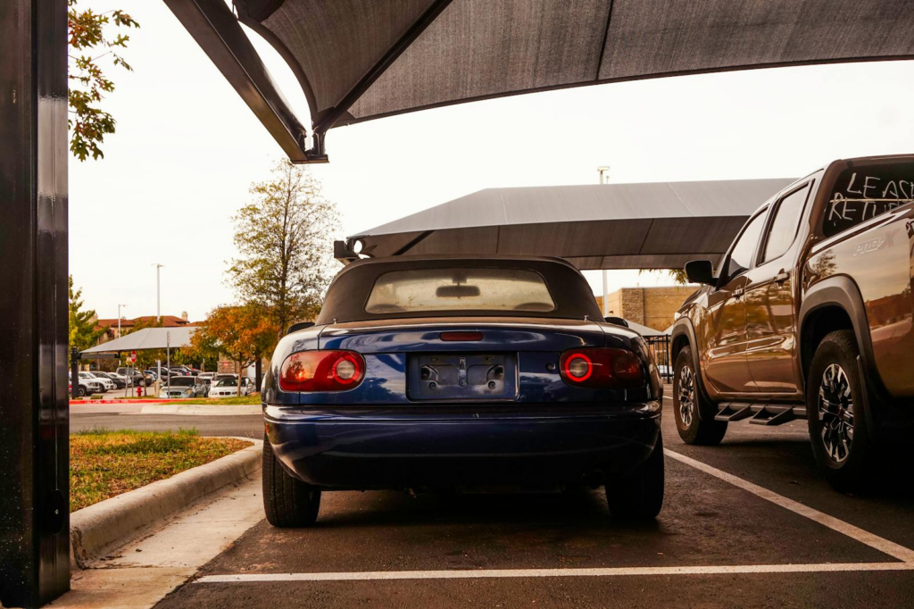 Rear view of a vintage blue convertible car parked beside a pickup in a city parking lot.