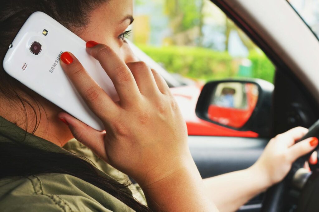 Close-up of a woman driving a car while talking on a smartphone, highlighting road safety concerns.