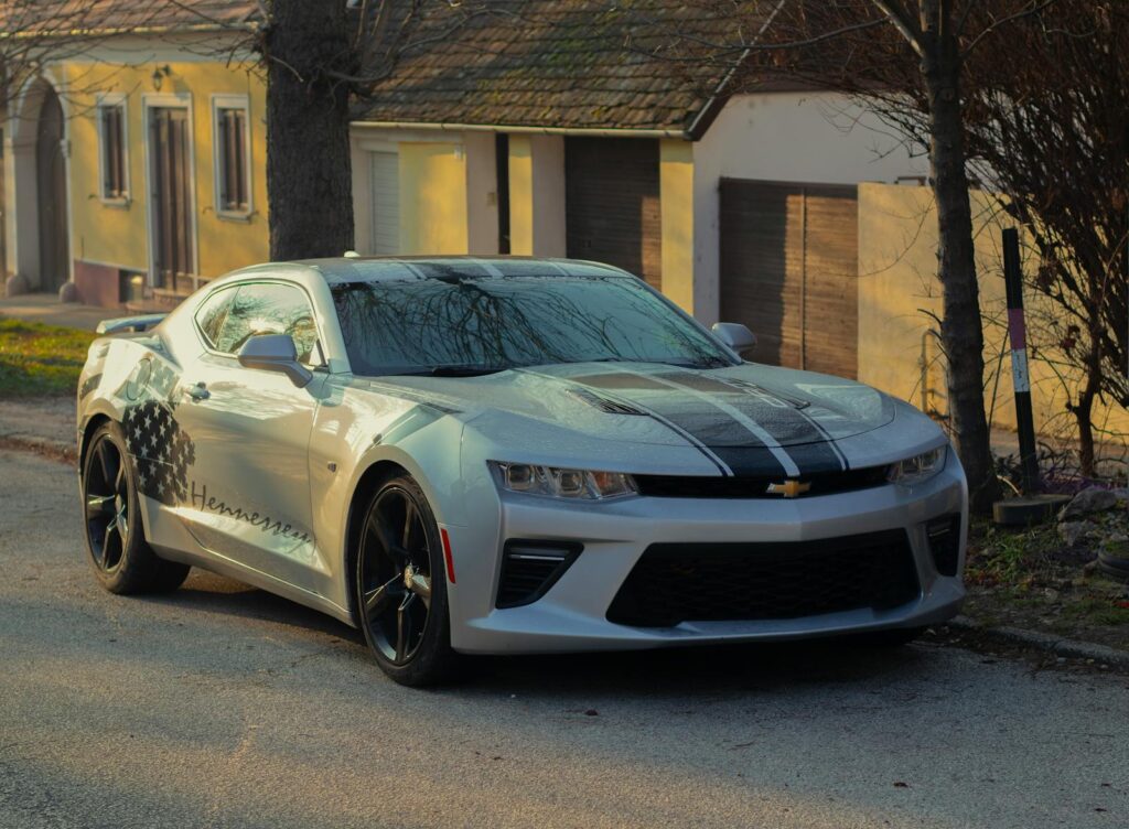 A stylish silver sports car with a stripe design parked in a quiet suburban street, casting a shadow.