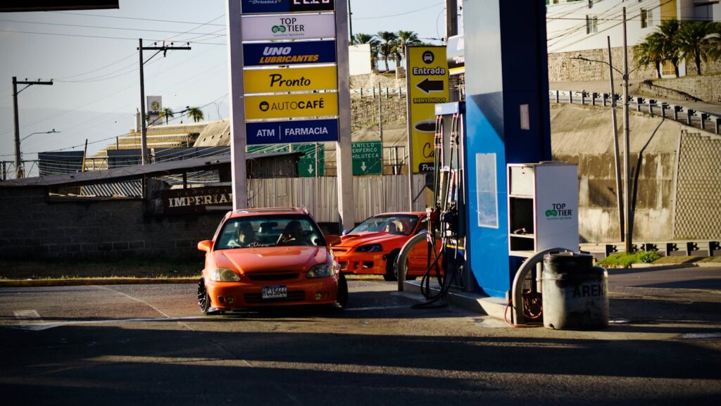 Two red cars refueling at a gas station under bright daylight.