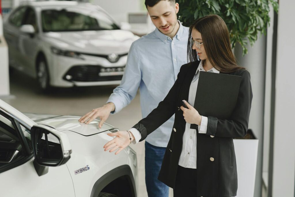 A man and saleswoman discussing a hybrid vehicle's features in an indoor showroom.