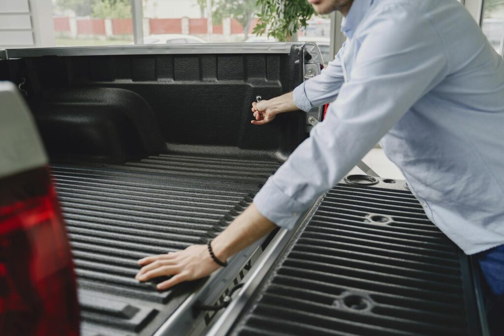 A man in a blue shirt opens the bed of a truck in a brightly lit indoor space.
