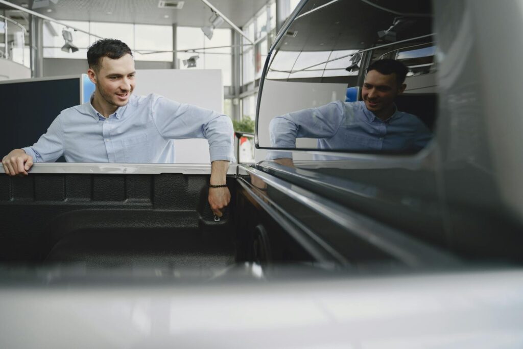 Man in a showroom examining the bed of a pickup truck, reflecting natural curiosity.