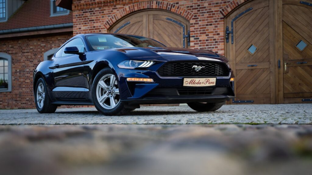 Low angle shot of a black Ford Mustang parked in front of a rustic brick building.