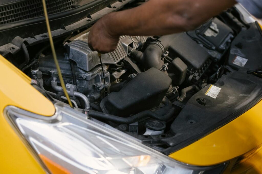 High angle of crop unrecognizable ethnic male cab driver checking contemporary bright vehicle hood in sunlight