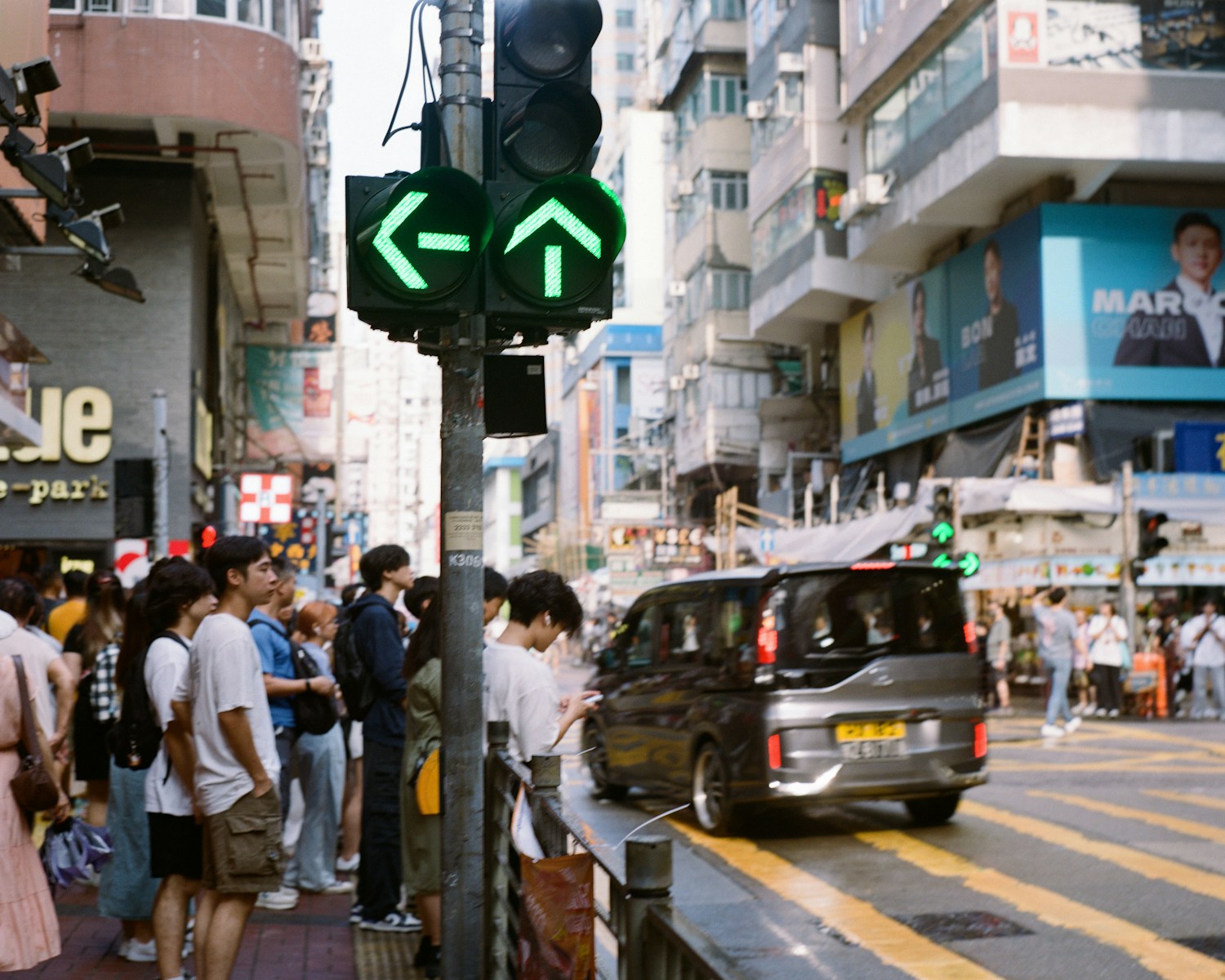 A group of people standing on a sidewalk next to a traffic light