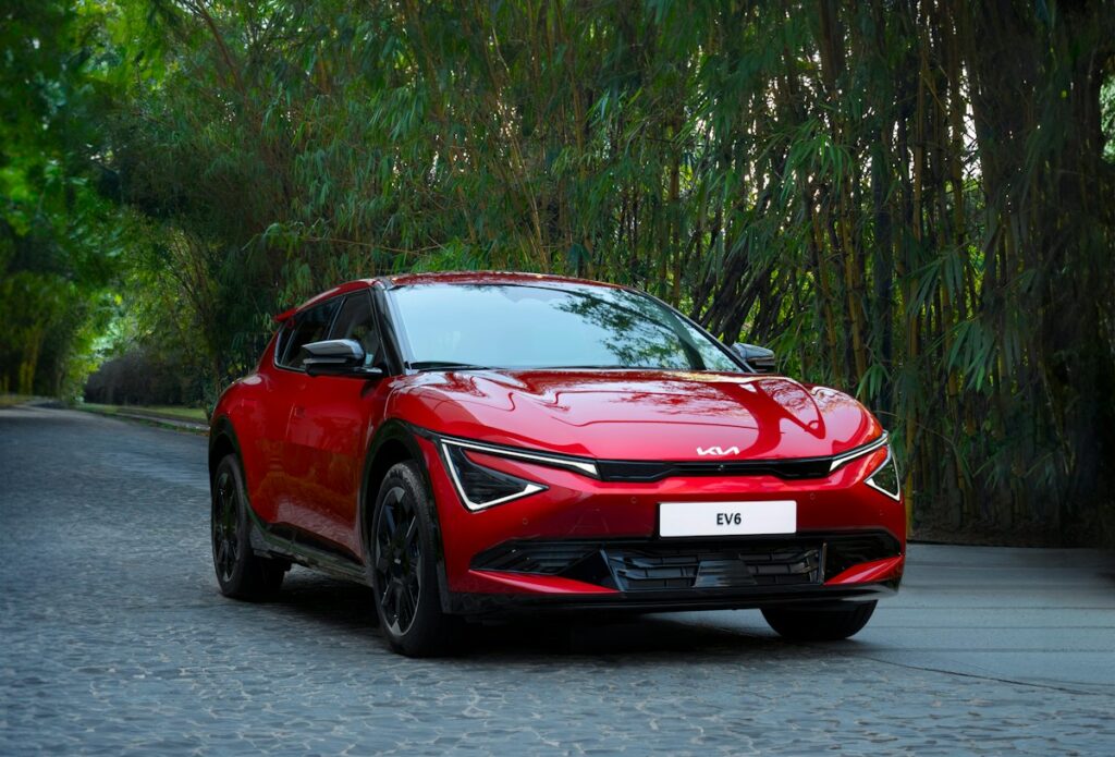 A red car driving down a street next to trees