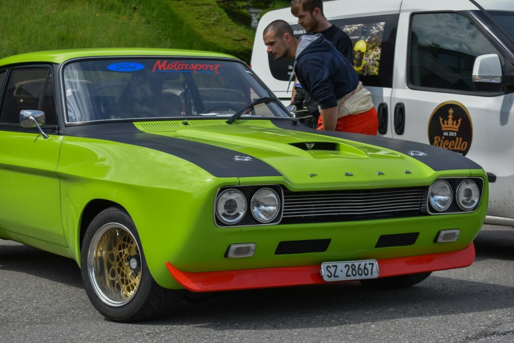 a green car with black stripes parked next to a white van