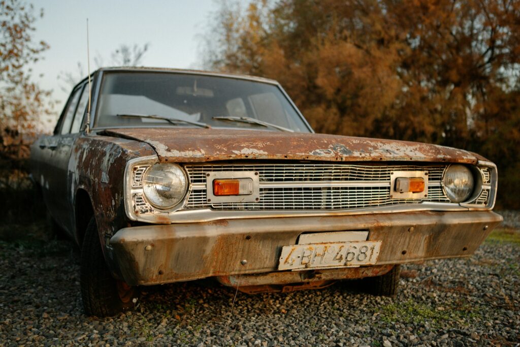A rusted out car sitting on top of a gravel field