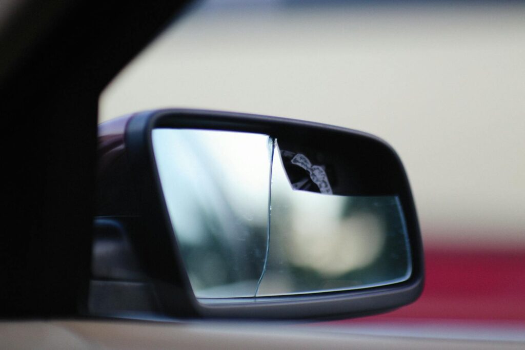 Close-up view of a cracked car side mirror reflecting a blurry background.