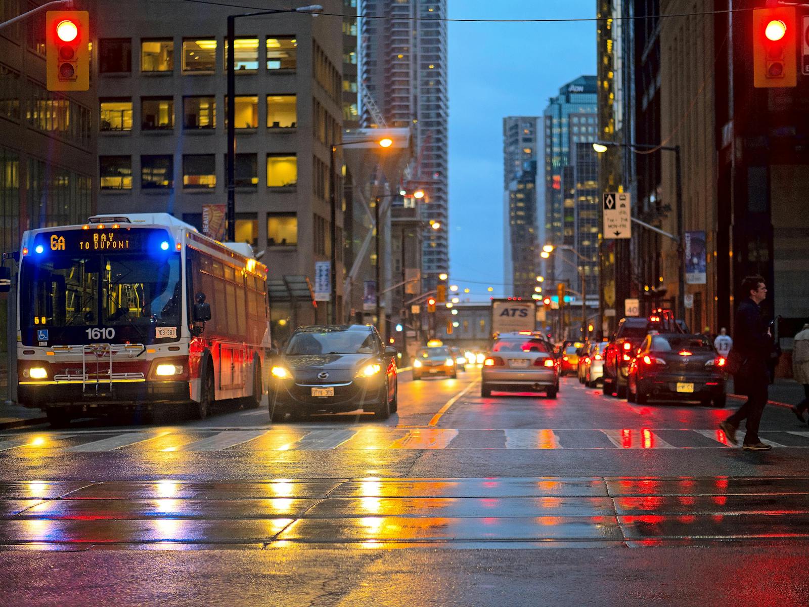 A bustling city street at night with vehicles, streetlights, and wet reflections.