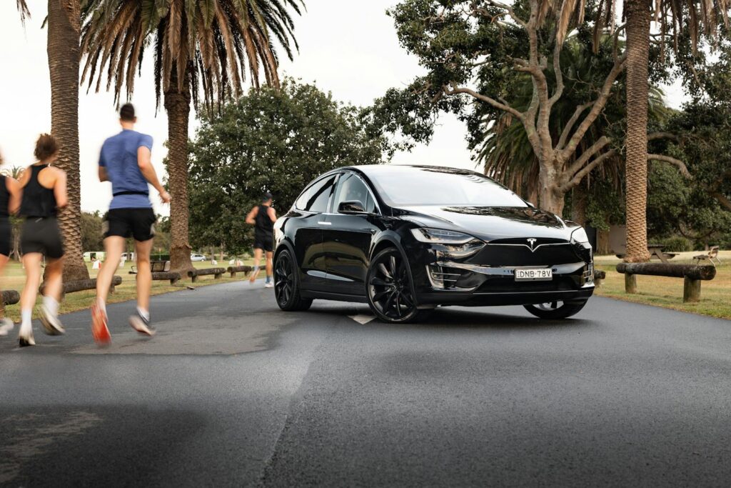 A sleek Tesla Model X parked on a road lined with palm trees in Sydney, showcasing modern automotive design.