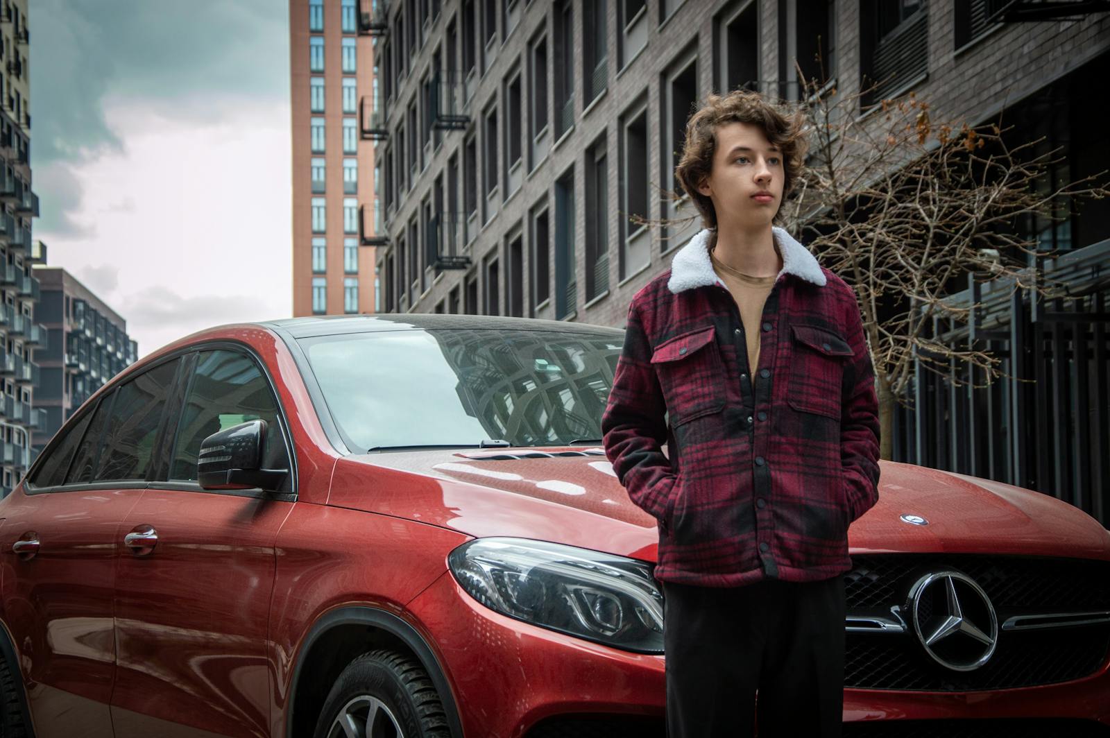 Teenager standing by a red sports car in a city street, urban lifestyle.