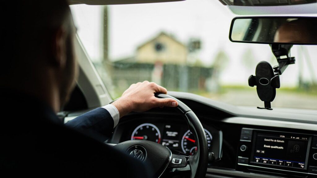 Businessman in suit driving a car, focus on steering wheel and dashboard.
