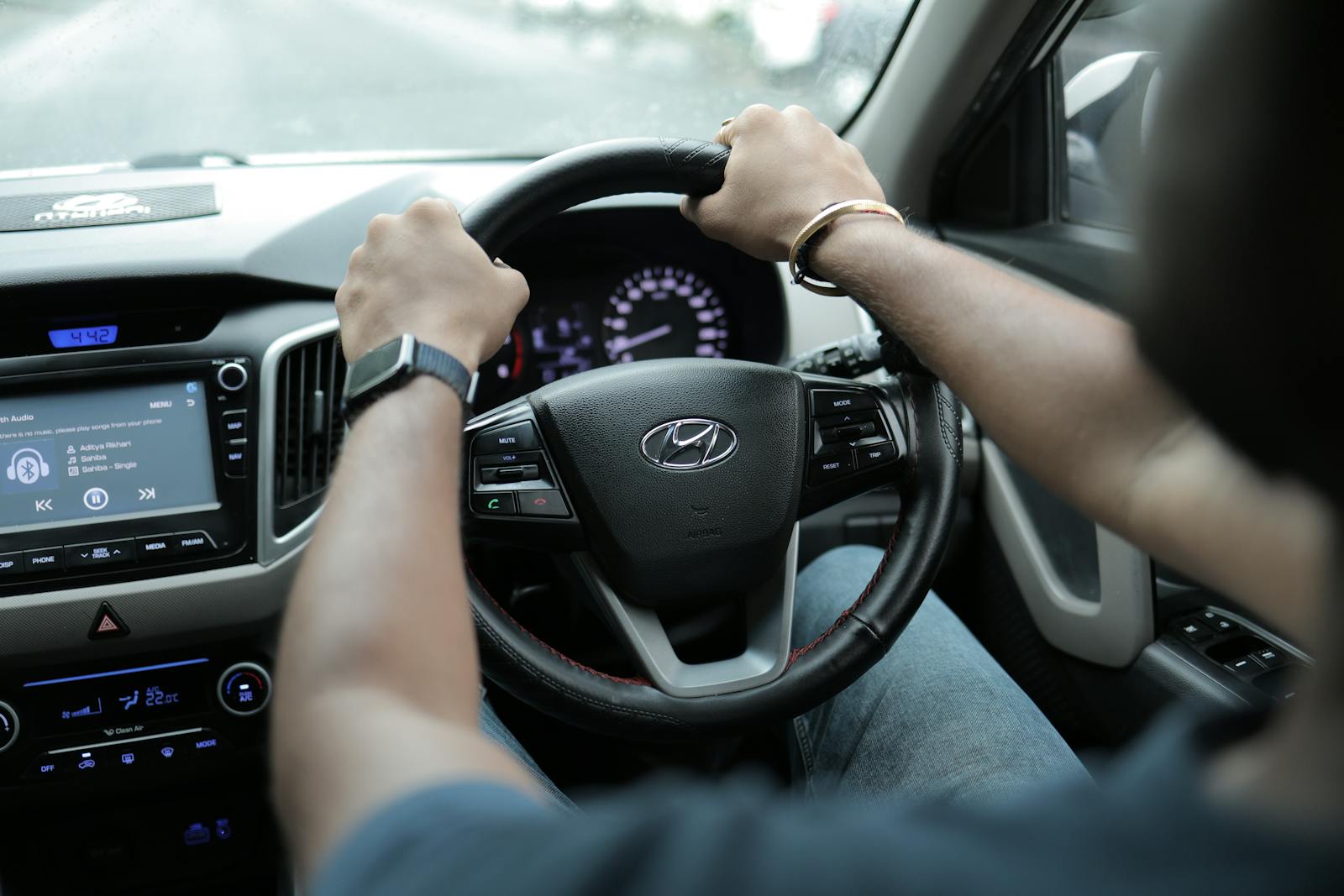 Close-up of a person's hands on a car steering wheel, highlighting the dashboard and interior features.