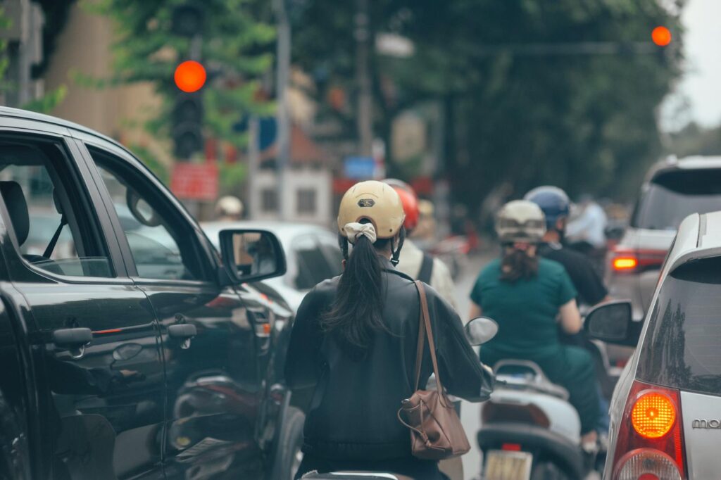A crowded city street with motorbikes and cars stopped at a red traffic light, depicting urban congestion.