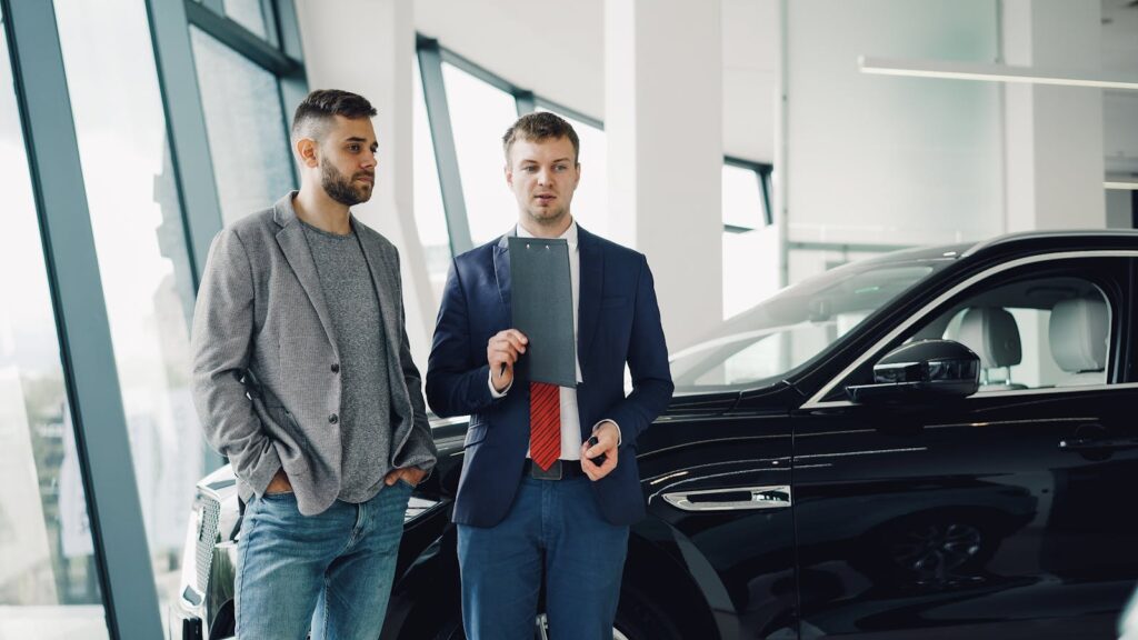 Two businessmen discussing car purchase in modern dealership showroom.