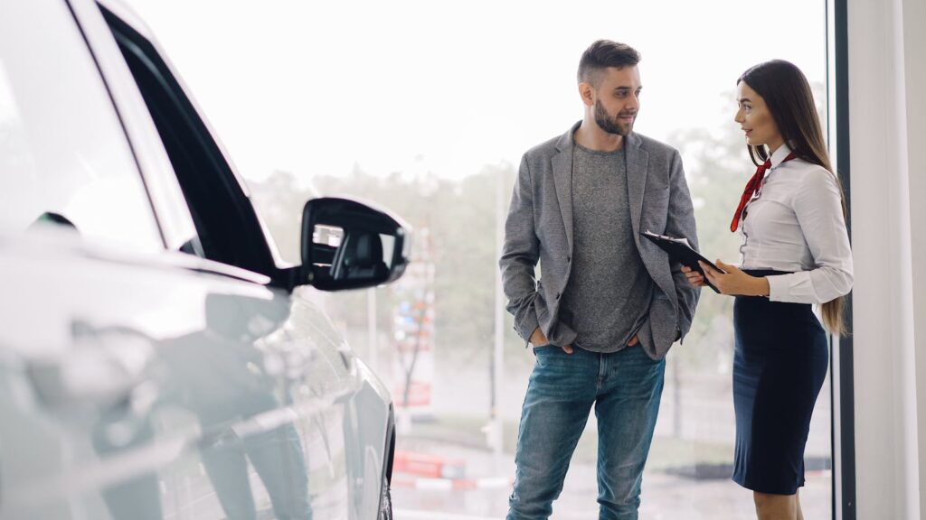 Man consulting with car salesperson in a showroom, discussing car options.