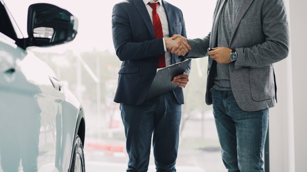 Two men shaking hands in a car dealership, symbolizing a successful business deal.