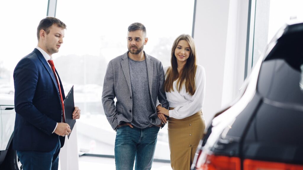 Smiling couple with salesman in car showroom discussing features of a car.