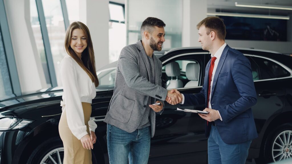 Buyers and sales representative shake hands at a car dealership for a successful car purchase.
