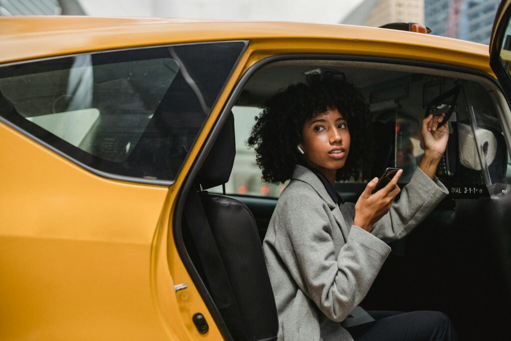Side view of charming black female in casual clothes holding smartphone while getting out of taxi