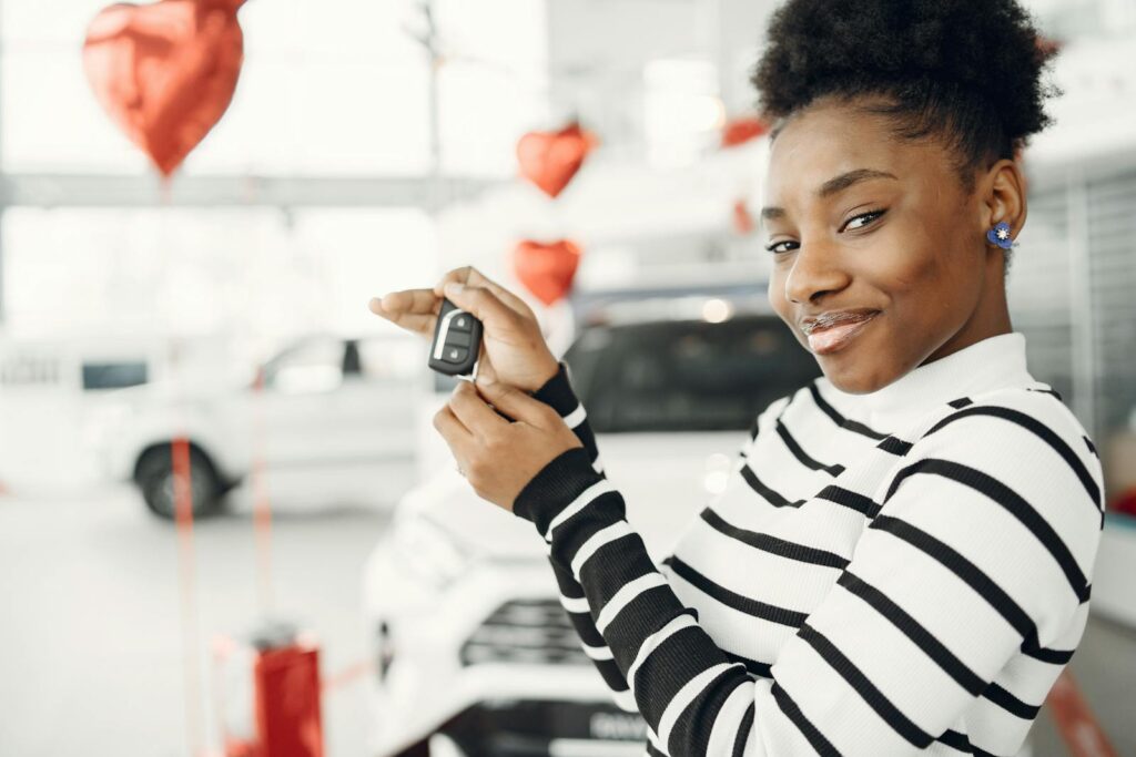Young woman with car key in a dealership, enjoying a new purchase.