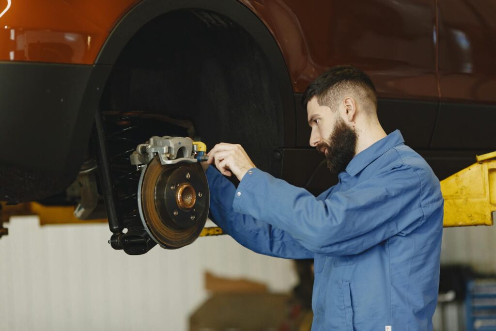 Mechanic in blue uniform performing brake repair on car in modern garage.