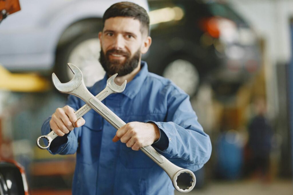 Mechanic in blue uniform holding wrenches inside an auto repair shop, ready for vehicle maintenance.