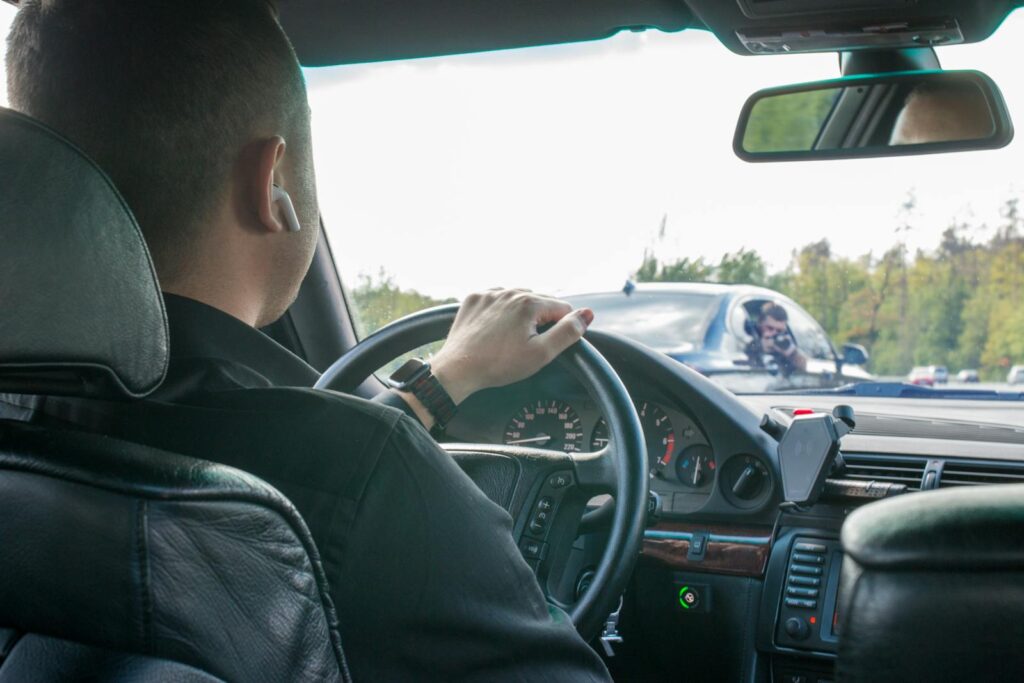 A man is driving a car seen from the back seat, focusing on the road ahead.