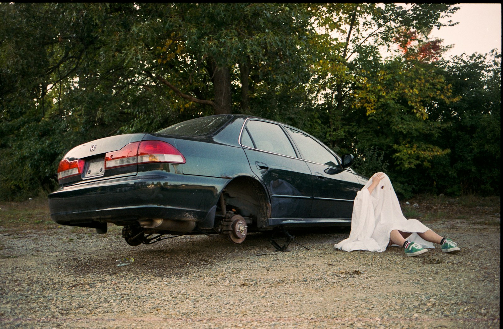 Person in sheet sits by car with no wheels.