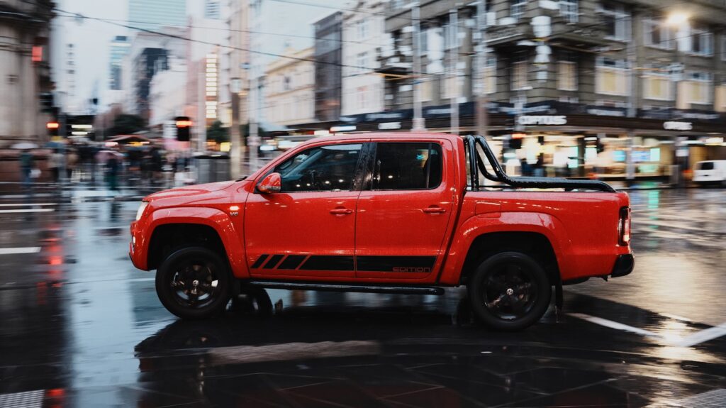 Red pickup truck driving on a wet city street