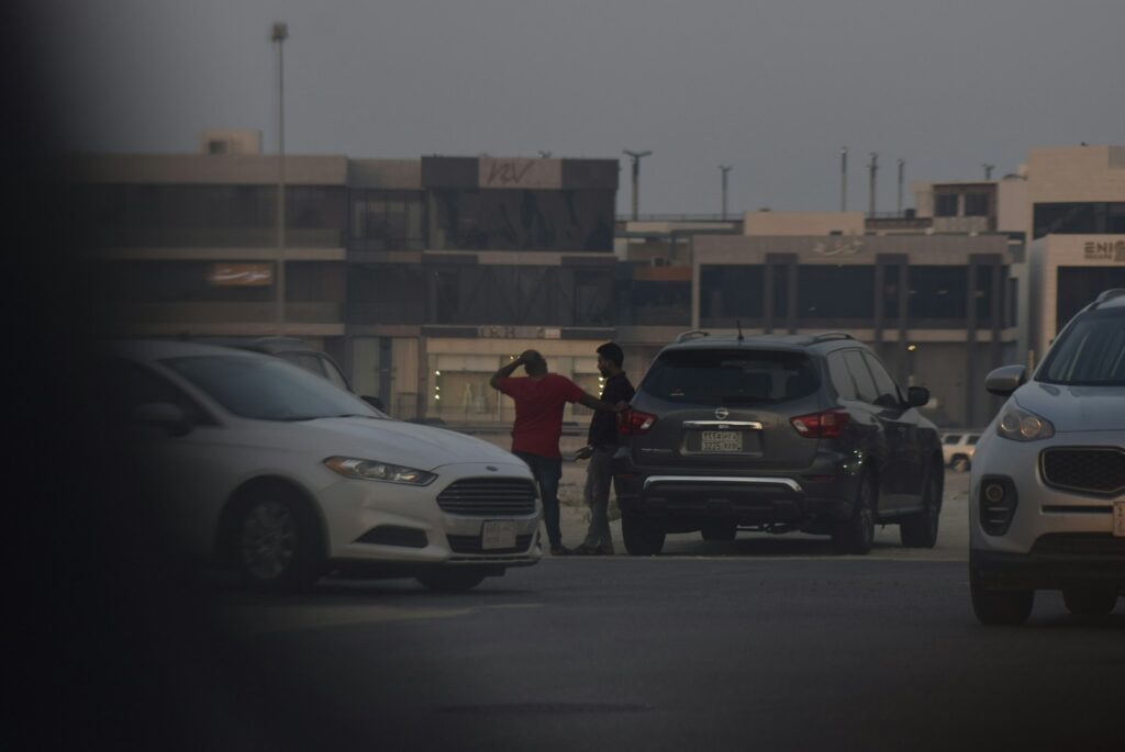 Two men standing between cars on a street.