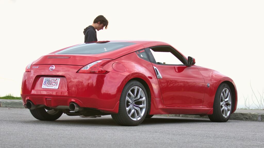 A young man leans out of a red sports car.