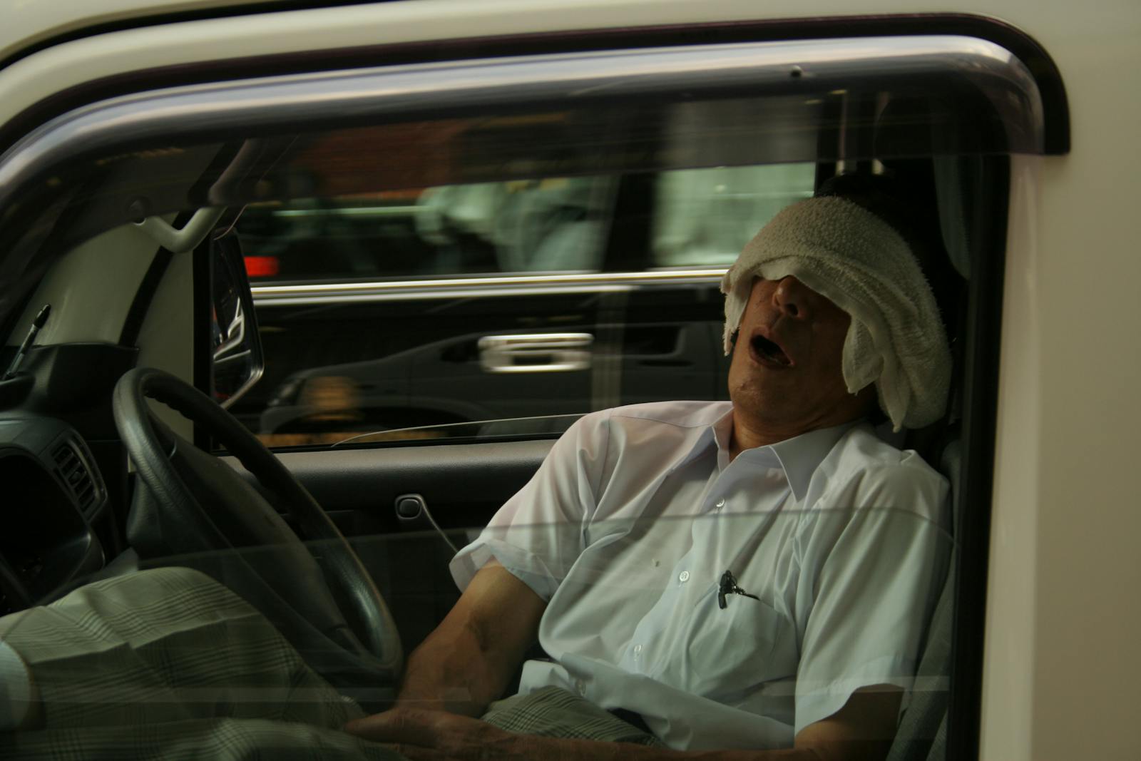 A man naps in his car with a towel over his eyes in bustling Tokyo, Japan.