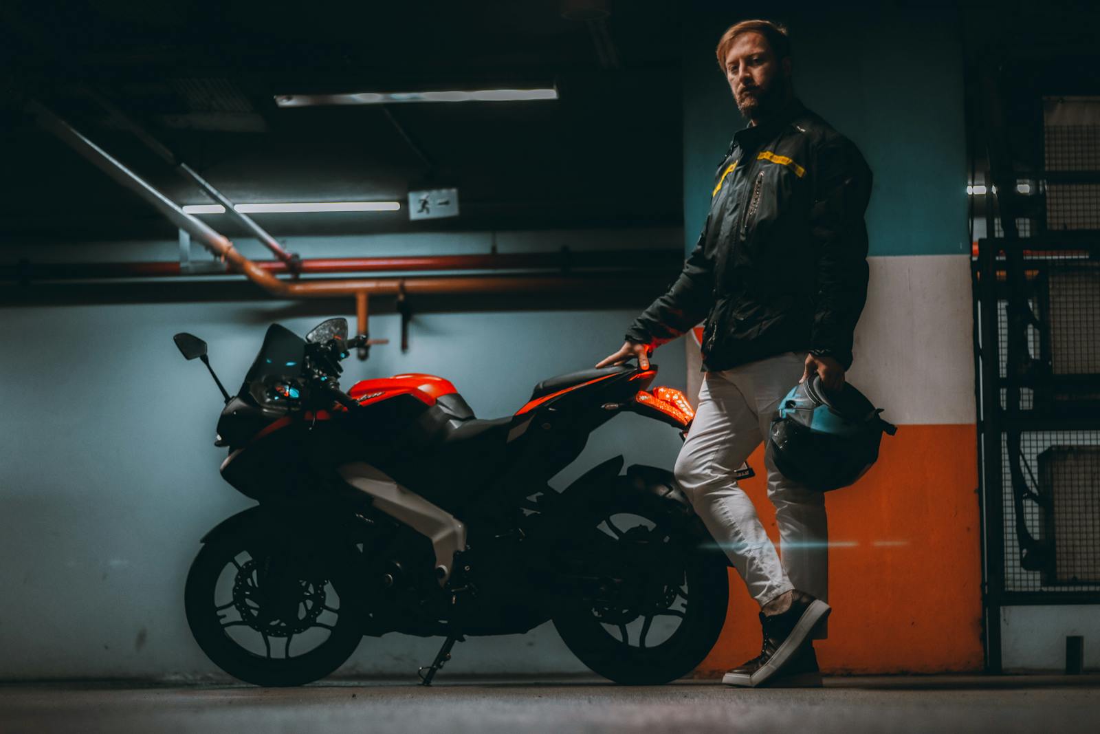 A man holds a helmet beside his motorcycle in a dimly lit garage.