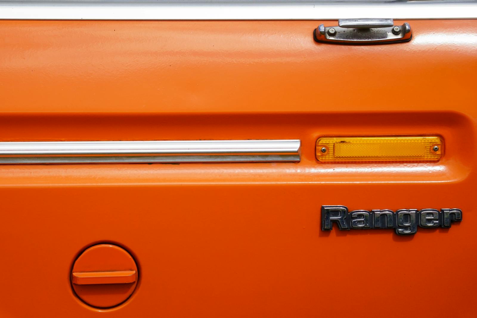 Detail shot of an orange vintage pickup truck tailgate with emblem and reflector.