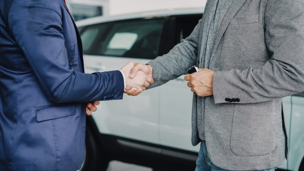 Two businessmen shaking hands in a car dealership, sealing a deal.