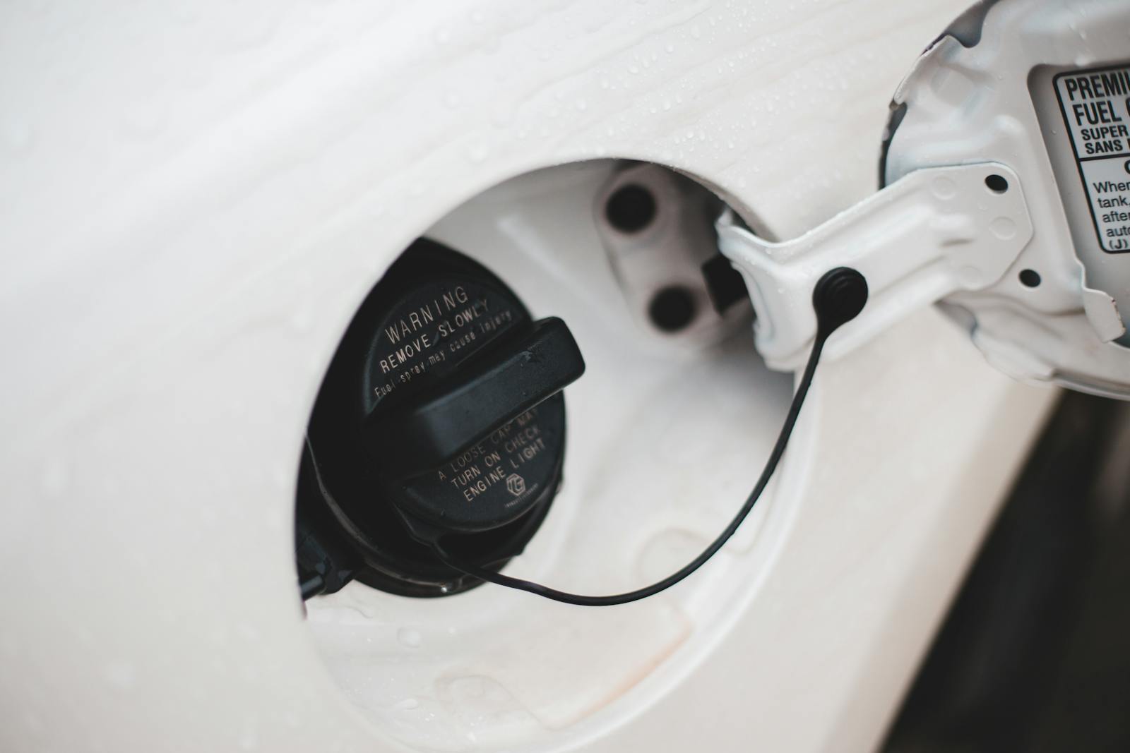 Black lid of petrol tank with titles and wire in contemporary white automobile in daytime