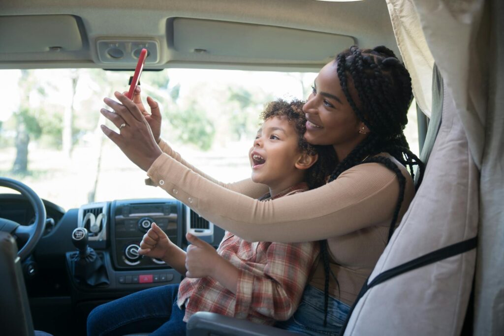 Happy mother and son enjoy a fun selfie moment inside a campervan, capturing a vacation memory.