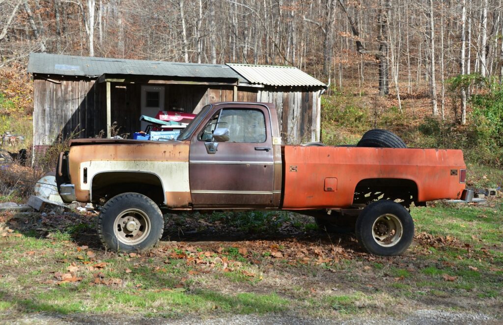 A rusted truck parked in front of a shed