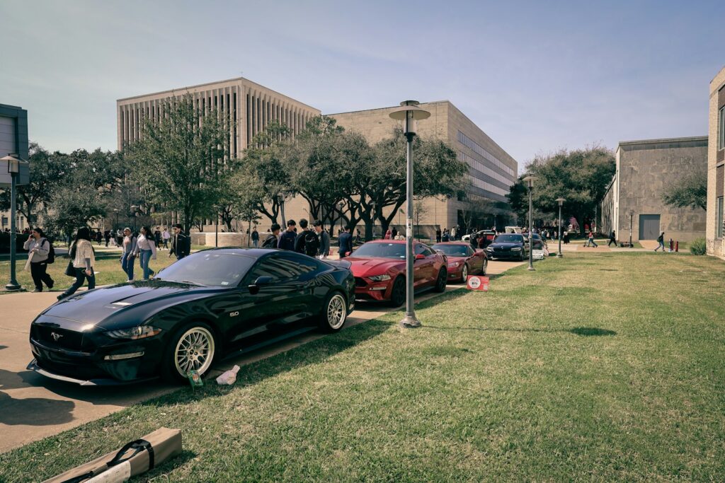 Several cars parked on a grassy area near buildings.